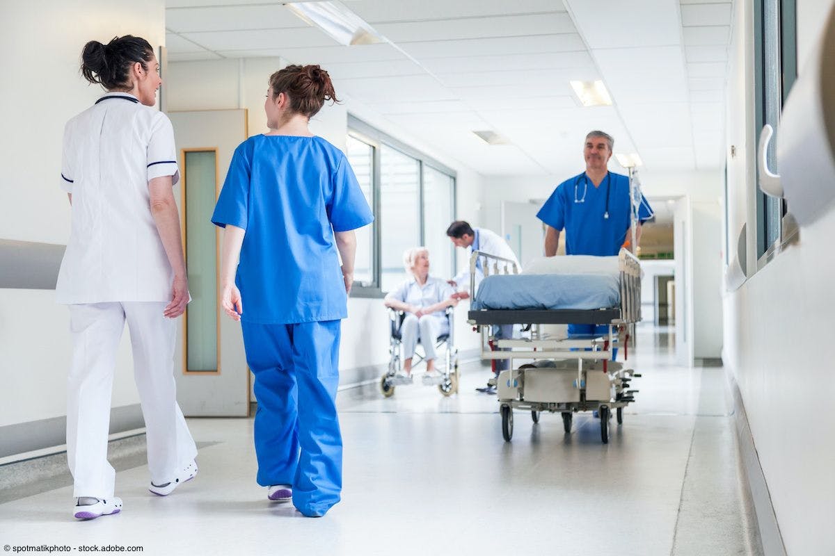 male nurse pushing gurney bed down hospital corridor. Also featured are female doctors and a senior female patient